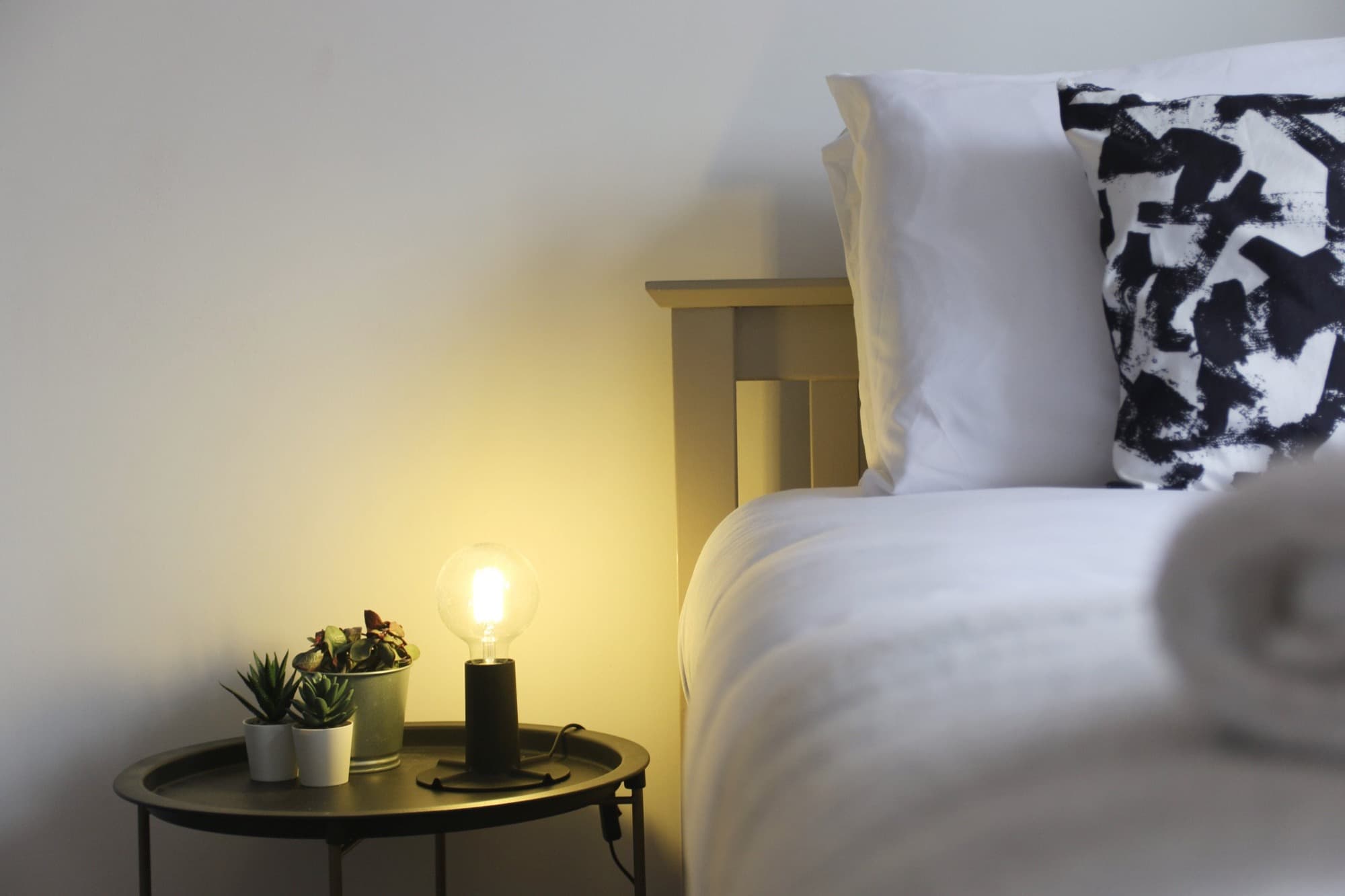 Bedside table with a warm lamp and succulents beside a freshly made bed in a Gough Groves managed short-let